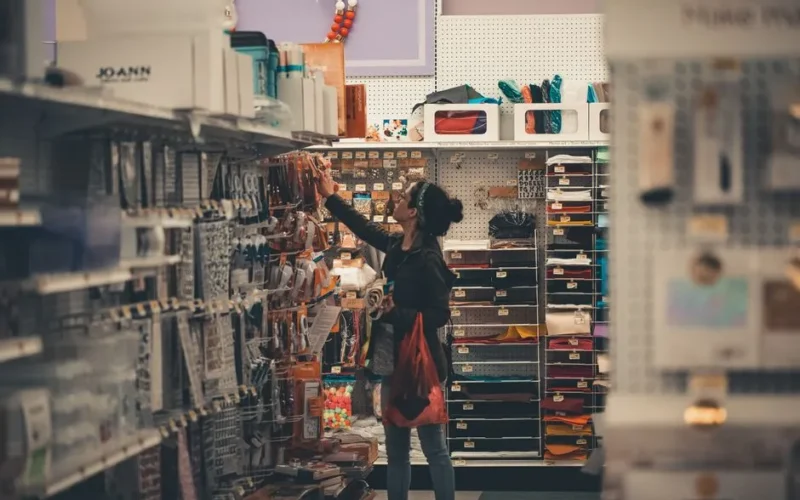 Woman reaching for items in a busy craft store aisle, exploring various art supplies.