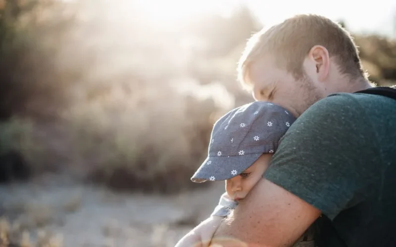 A father lovingly embraces his baby outdoors on a sunny day. Perfect for Father's Day themes.
