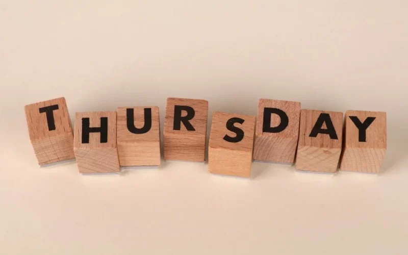 Wooden blocks arranged to spell Thursday on a neutral background.