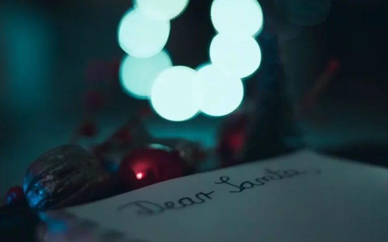 Festive image of a handwritten 'Dear Santa' letter with Christmas decor and blurred lights.