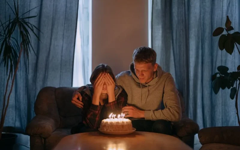 Two friends sharing a heartfelt birthday moment with a cake and candles indoors.