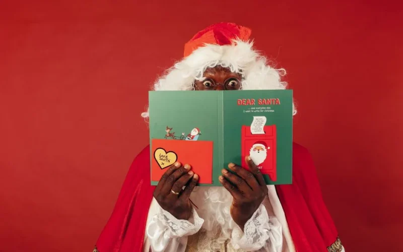 Santa Claus holding a Christmas card with a surprised expression against a red background