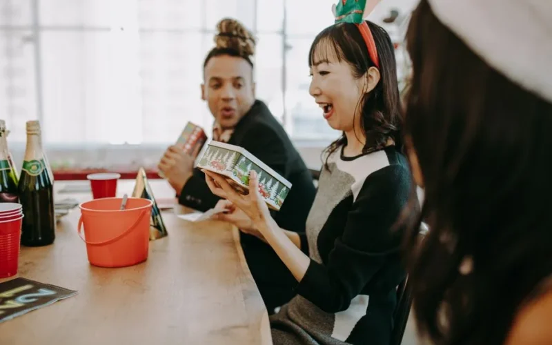 A joyful team enjoys a Christmas party with gifts at an office setting.