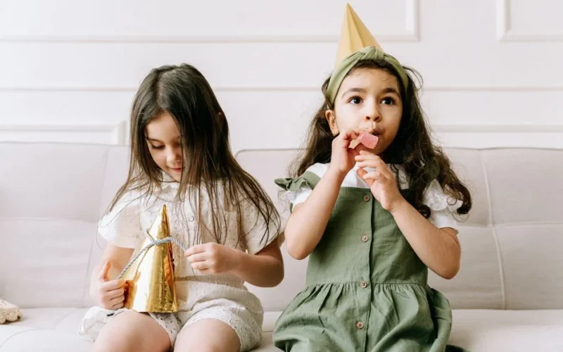 Two young girls in party hats enjoying a birthday celebration indoors.
