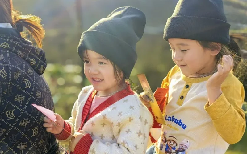 Two children in beanies enjoying a sunny day, holding cards and playing.