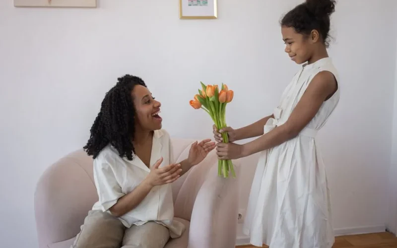 A daughter surprises her mother with a bouquet of tulips at home, capturing love and happiness.