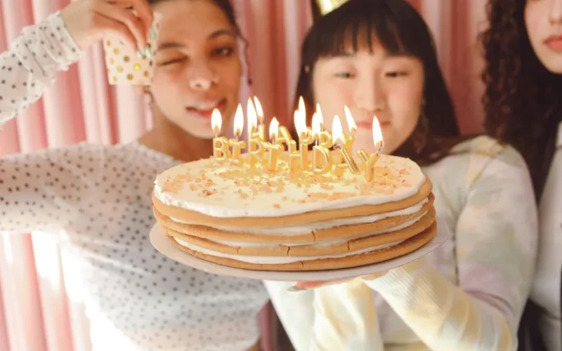 A joyful birthday party scene with teenagers holding a cake with lit candles.