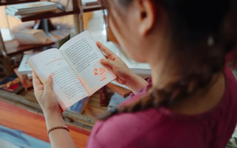 A girl with braided hair reads a book in a cozy library environment.