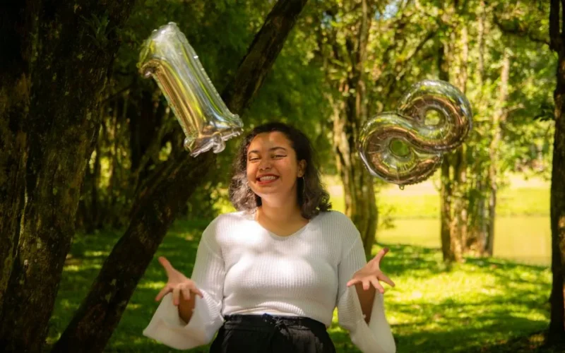 Smiling woman celebrating her 18th birthday outdoors with metallic balloons.