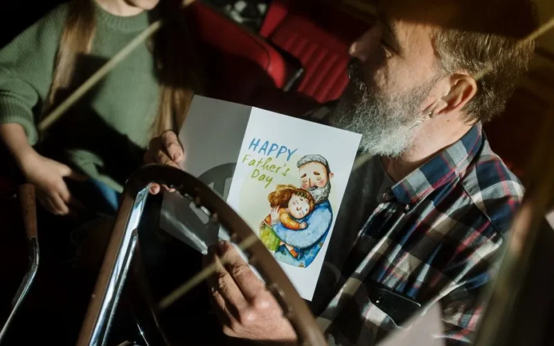 Father holding a Father's Day card inside a car, enjoying quality time with daughter.