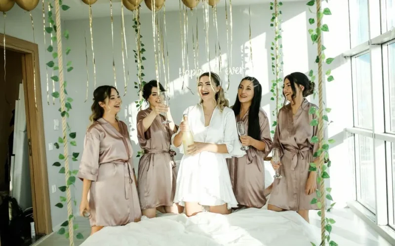 Bride and bridesmaids celebrating with champagne indoors. Joyful wedding preparation moment.
