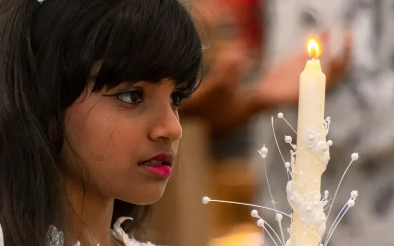 Serene young girl holding a beautifully decorated candle during a solemn ceremony.