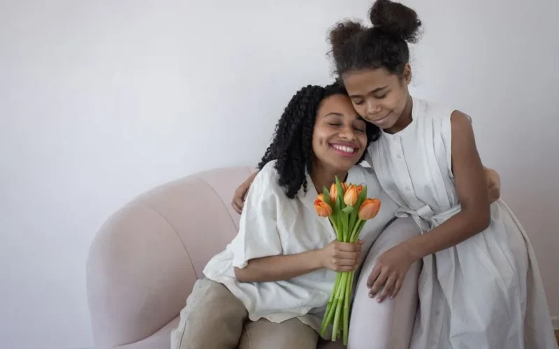 A heartwarming scene of a mother and daughter hugging with tulips, capturing love and bonding indoors.