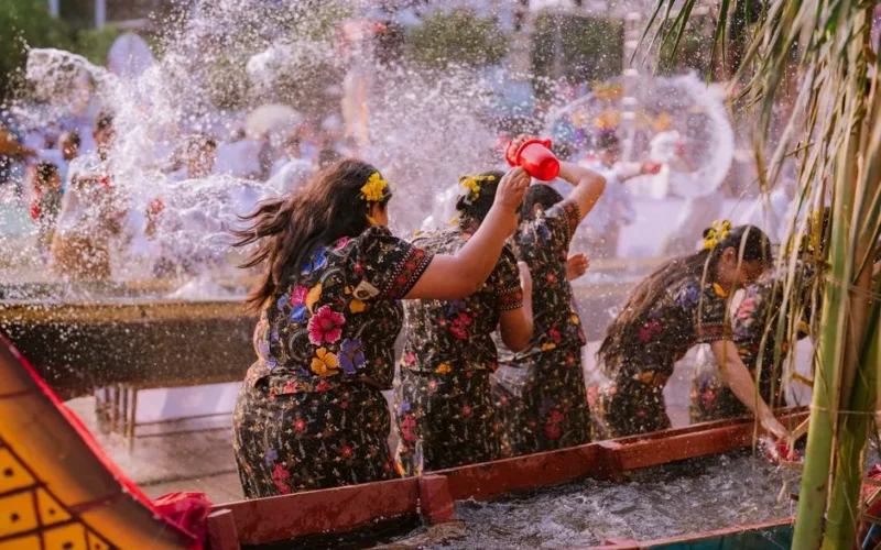 Colorful cultural water festival with women in traditional attire playfully splashing water.