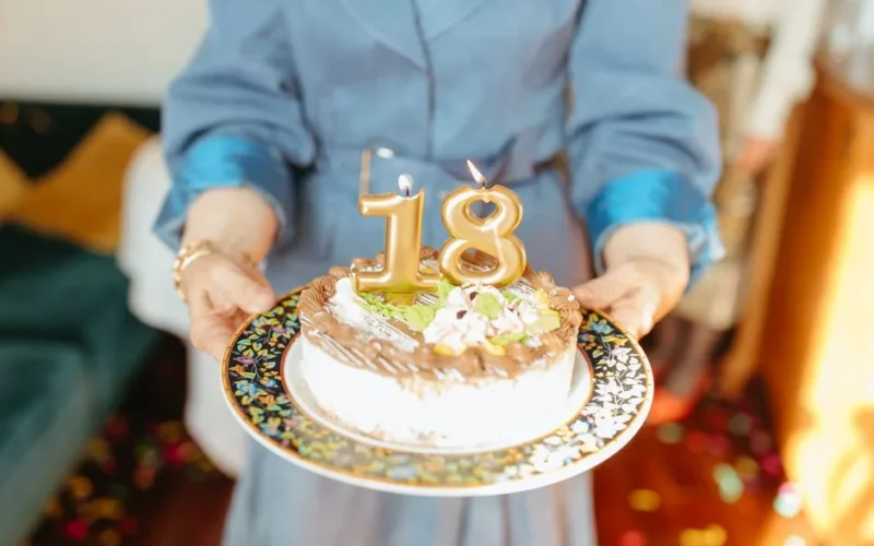 Close-up of hands holding a birthday cake with '18' candles for a celebration.
