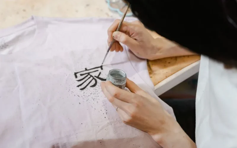 Artist hand painting calligraphy on a t-shirt, close-up view of creative process.