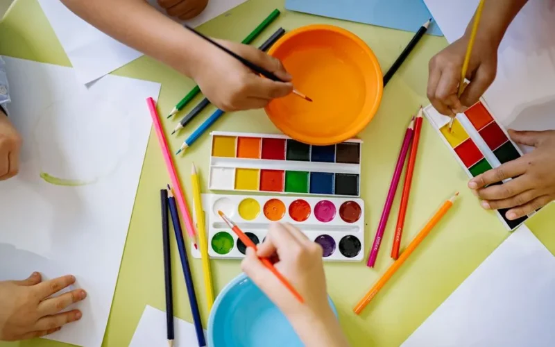 Children using watercolors and colored pencils for an art project, fostering creativity.