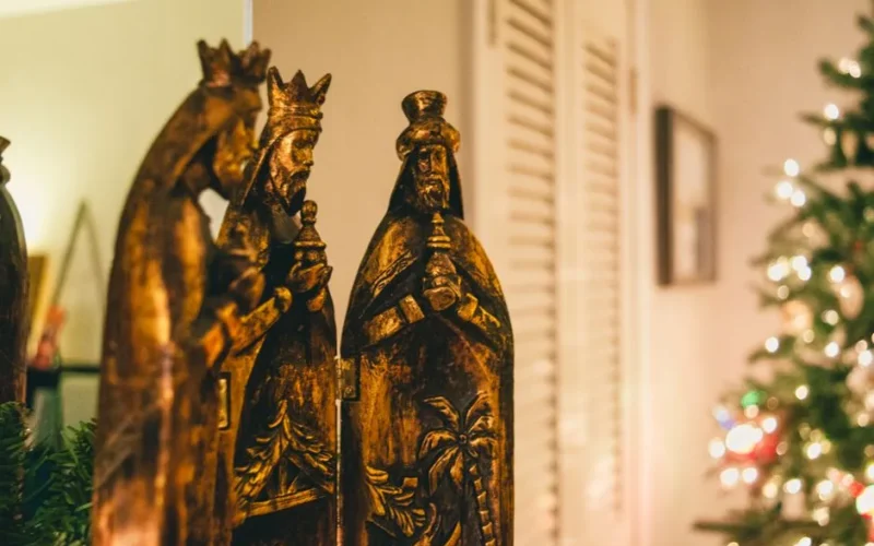 Beautiful traditional Three Kings figurines with blurred Christmas tree lights in the background.