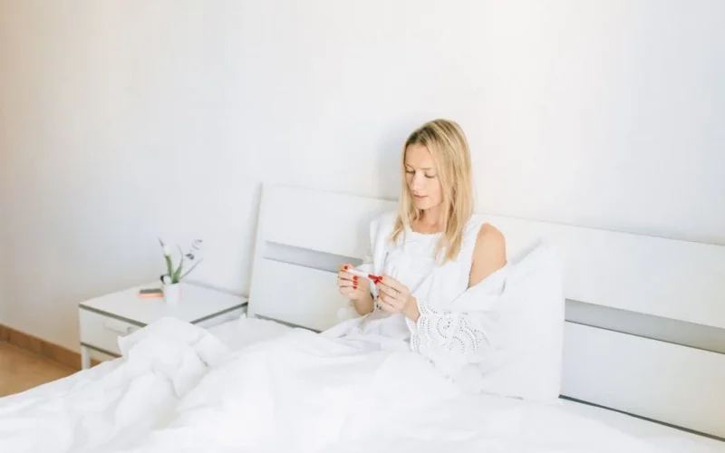 Woman sitting in bed examining a pregnancy test, conveying anticipation and hope.