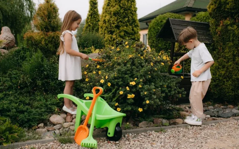 Kids playing with gardening tools among blooming flowers in a vibrant backyard setting.