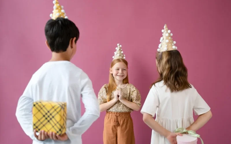 Joyful children celebrating a birthday with hats and gifts in a lively indoor setting.