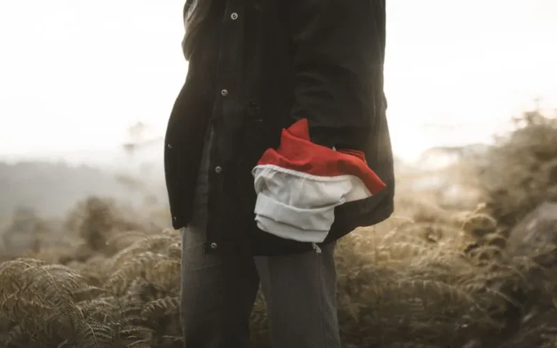 A person holding red and white fabric, standing outdoors in a natural setting.