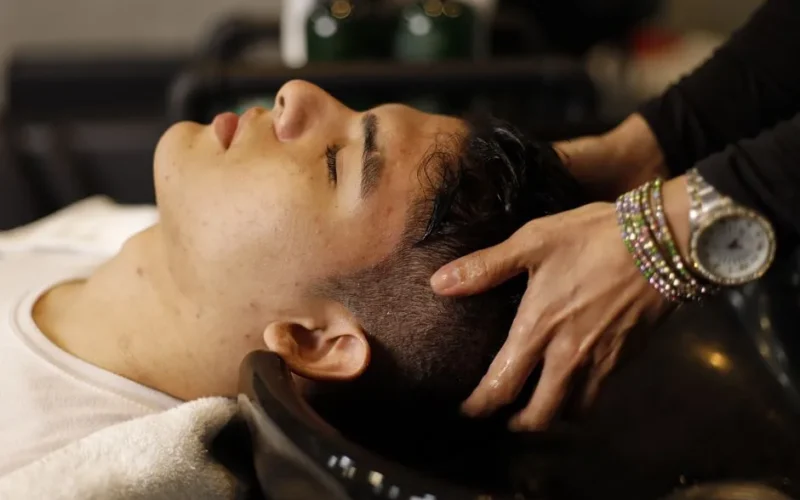 Man with closed eyes enjoying a relaxing hair wash at salon sink by a professional stylist.