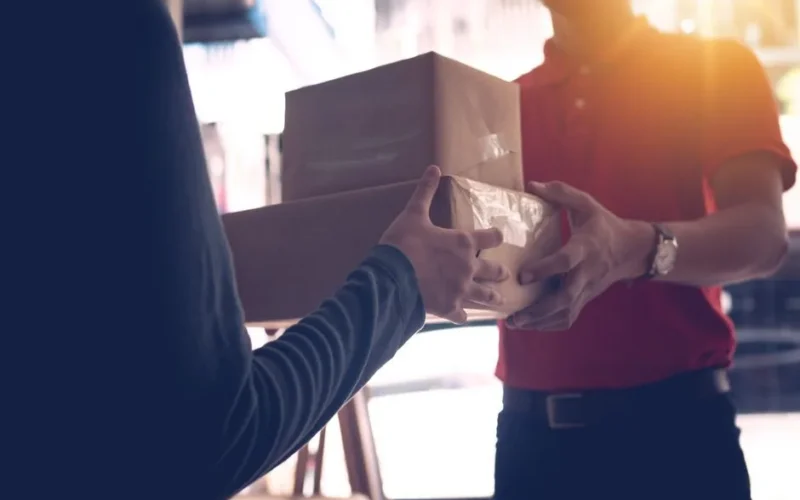 Close-up of a delivery service worker handing over packages to a customer indoors.