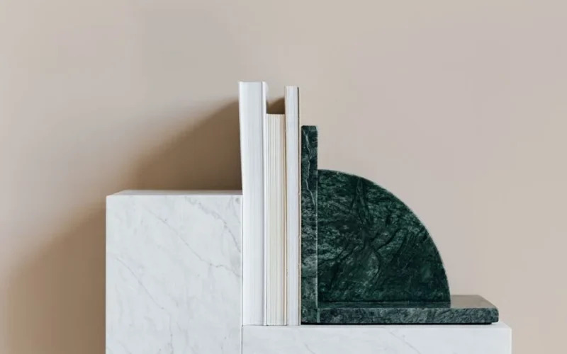 Green marble bookend with set of various books placed on geometric shelf against wall