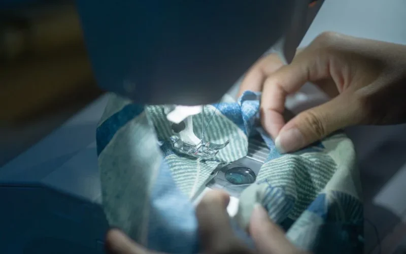 Hands guiding fabric through a sewing machine, showcasing precision and craftsmanship.