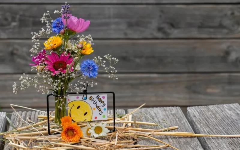 Vibrant floral bouquet with a birthday card on a rustic wooden table, perfect for celebrations.