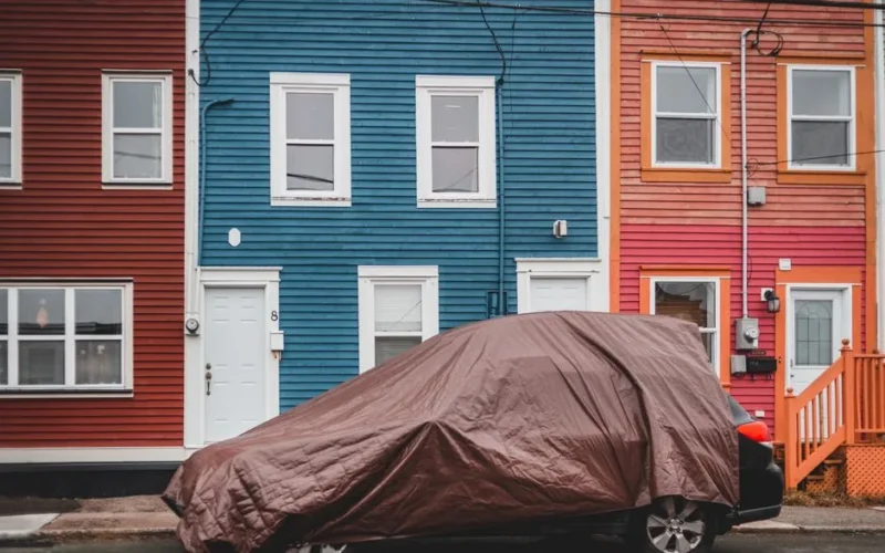 Automobile covered with brown fabric parked on road near colorful residential houses with windows and doors on street of town