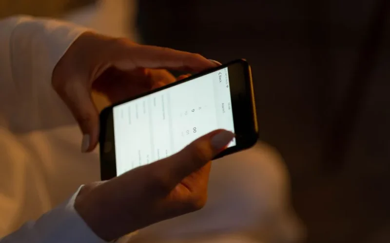 Close-up of hands setting an alarm on a smartphone, depicting night usage and technology interaction.