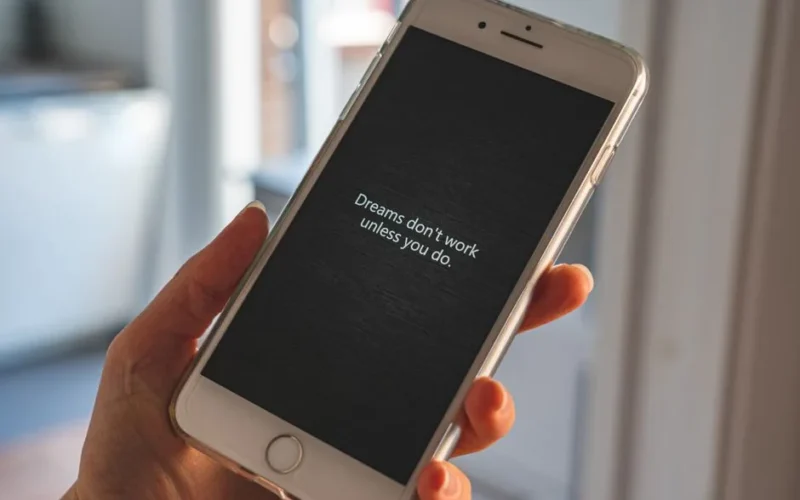 Hand holding smartphone displaying motivational quote: 'Dreams don't work unless you do.'