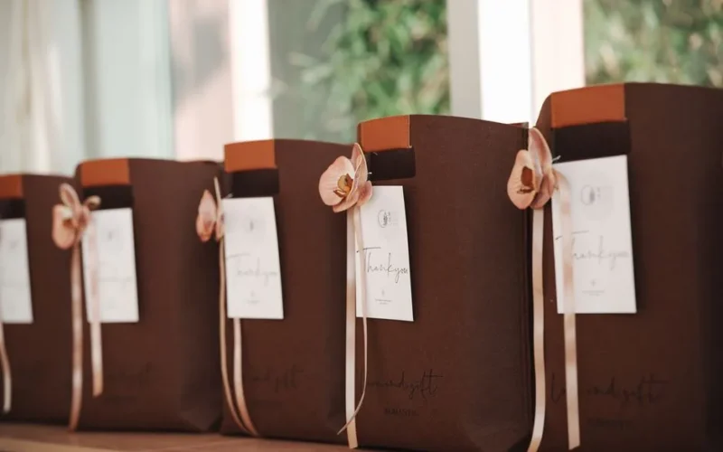 A row of elegant brown gift bags adorned with pink flowers and thank you notes, perfect for events.