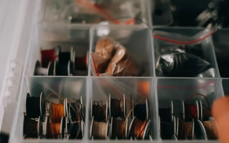 Close-up of assorted sewing threads in transparent organizer box for crafting and sewing projects.
