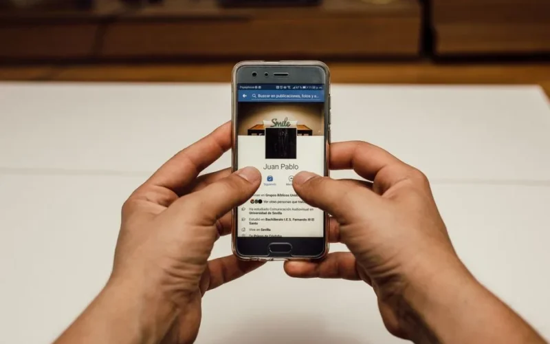 Close-up of hands using a smartphone with a social media page indoors.