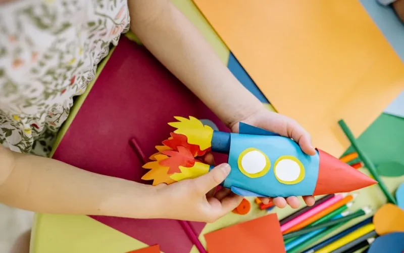 A child builds a vibrant paper rocket during an arts and crafts session, fostering creativity.
