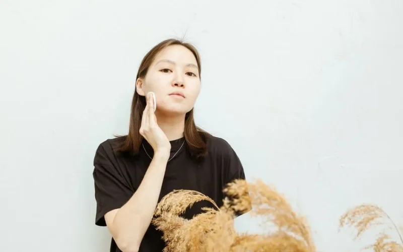 An Asian woman gently applies facial care in a calm, minimalist setting.