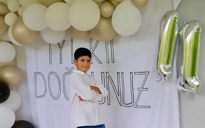 Boy celebrating 11th birthday with balloons and a festive banner backdrop.