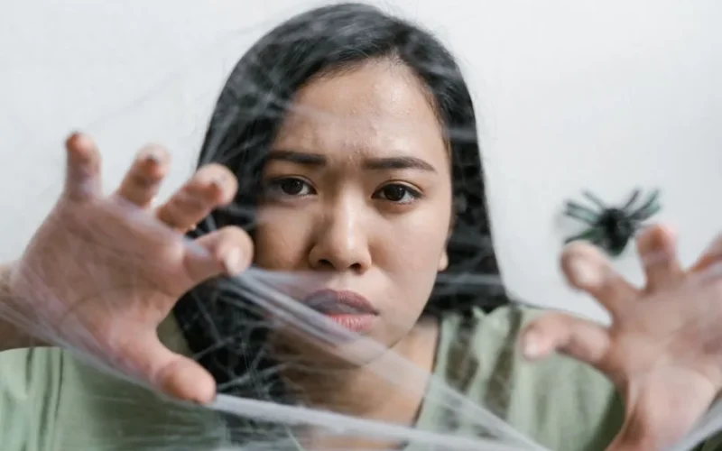 A woman faces anxiety symbolized by a spider web, conveying emotions of fear and entrapment.