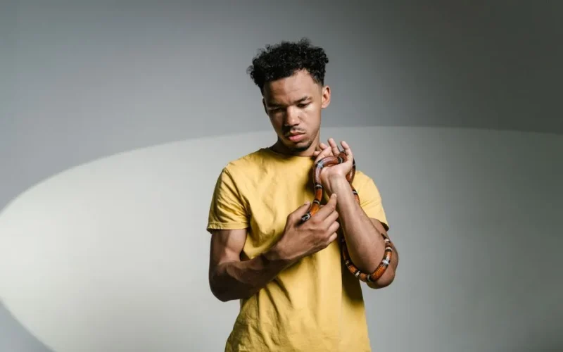 A young man holds a snake, overcoming ophidiophobia in a studio setting.