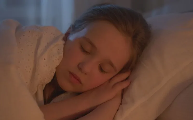 A young girl sleeping peacefully indoors, bathed in warm light.