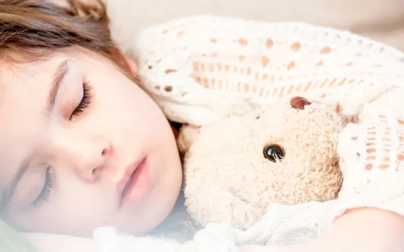 Peaceful child cuddling a teddy bear while sleeping, exuding warmth and security.