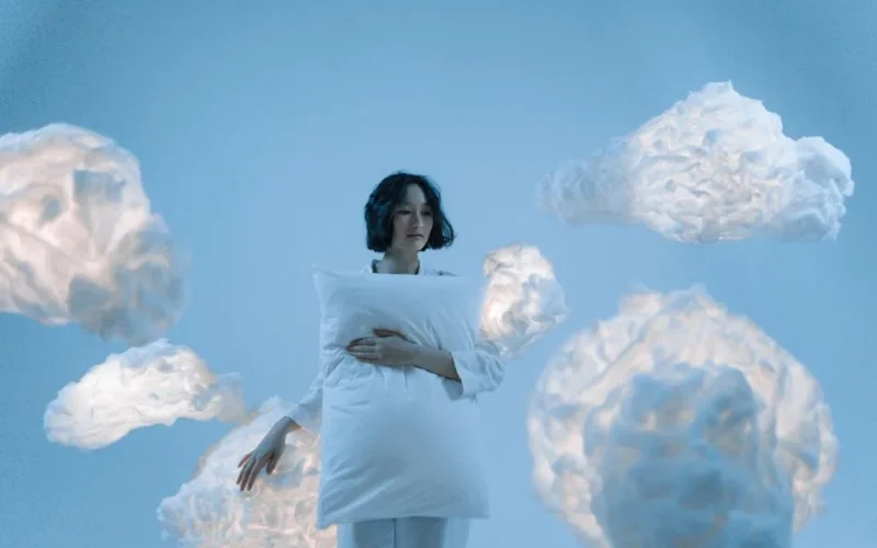 A serene portrait of a woman holding a pillow surrounded by soft clouds, evoking a dreamlike atmosphere.