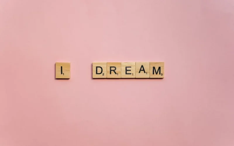 Scrabble tiles spelling 'I Dream' on a soft pink background for motivation.