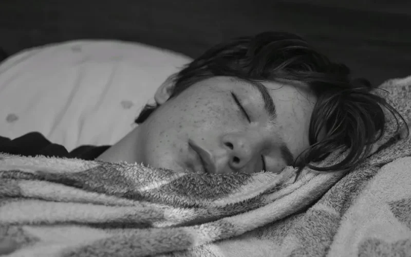 Black and white photo of a teenage boy sleeping peacefully wrapped in a blanket.