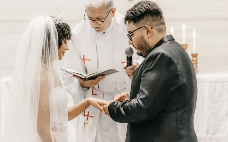 Bride and groom exchanging vows in a church ceremony led by a priest.
