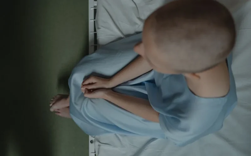 Bald patient sitting on hospital bed, expressing vulnerability and introspection.