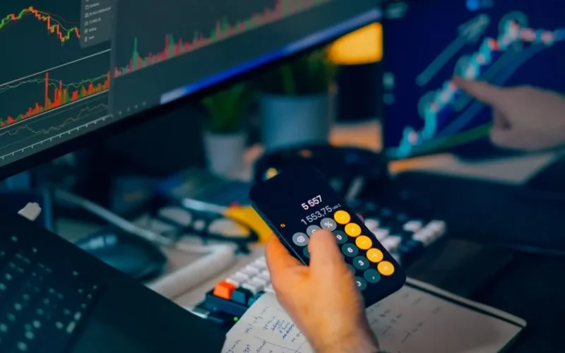 A focused shot of financial trading with screens, calculator, and data charts.
